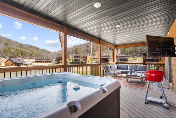 Un jacuzzi en una terraza de madera con vistas a casas al fondo.