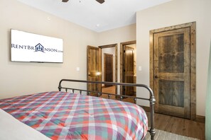 A bedroom with a bed, a television mounted on the wall, and wooden doors.