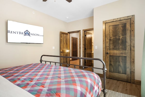 A bedroom with a bed, a television mounted on the wall, and wooden doors.