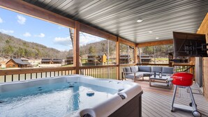 A hot tub on a wooden deck with outdoor furniture and a barbecue grill.