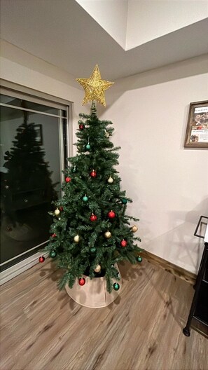 Un árbol de Navidad con una estrella en la punta en un rincón de una habitación con suelo de madera y un ventanal grande.