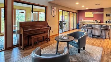 Amplia sala de estar con piano, asientos cómodos, zona de bar y ventanas grandes con vistas al exterior.
