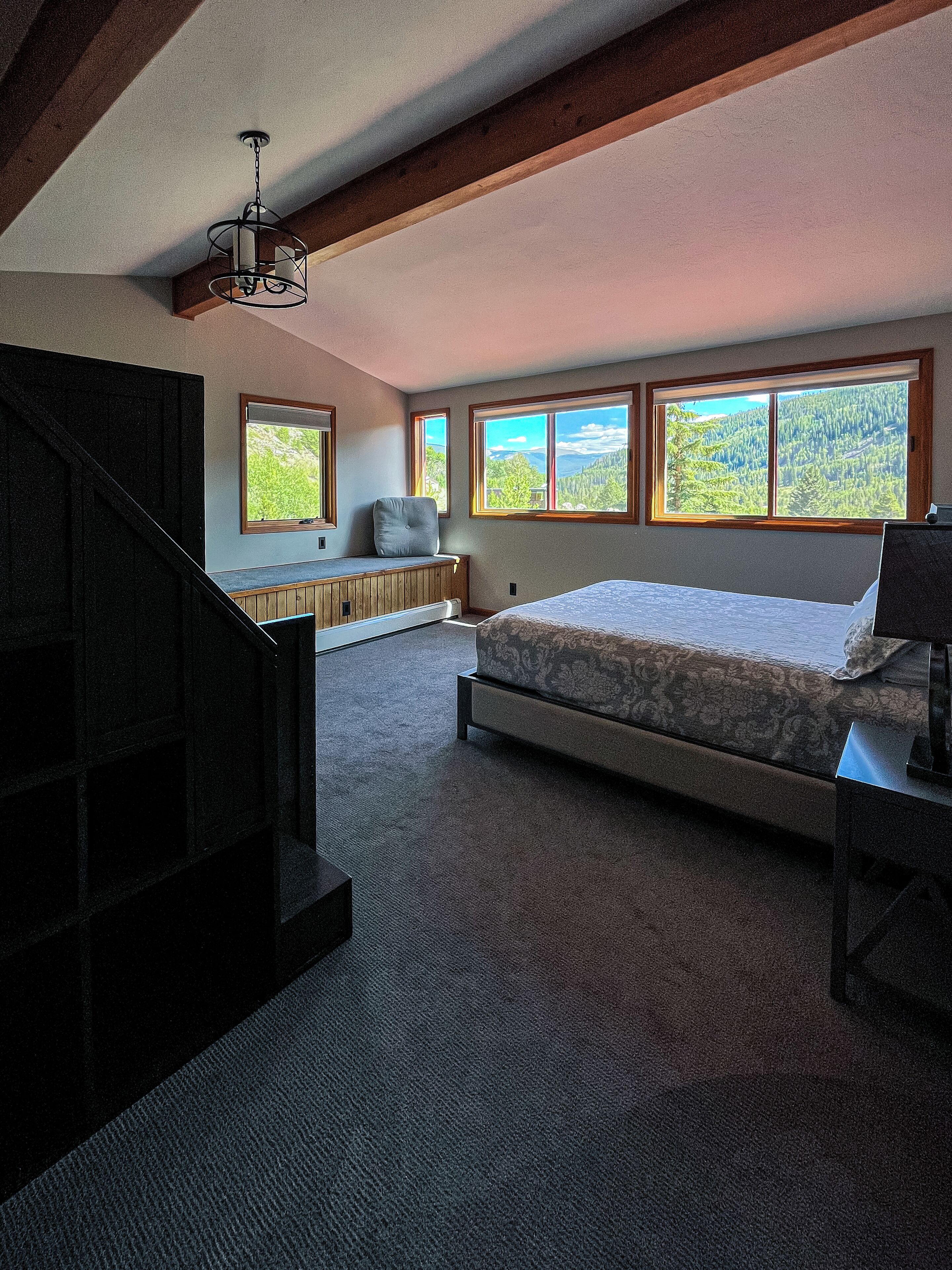 A bedroom with a large bed, a bench, and a view of a forest through large windows.