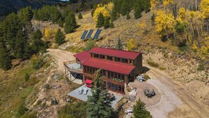 A modern two-story building with a red roof, surrounded by a natural landscape with trees and solar panels.