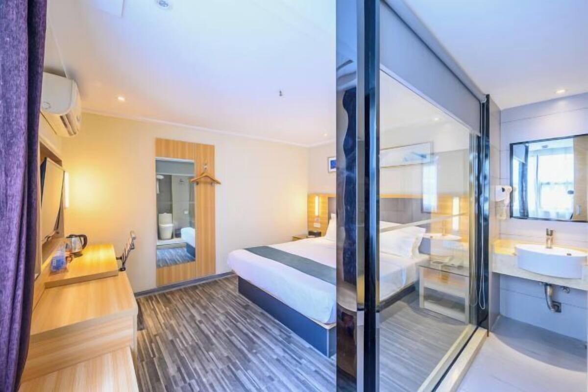 A modern hotel room with a bed, bedside table, and a glass-enclosed shower area.