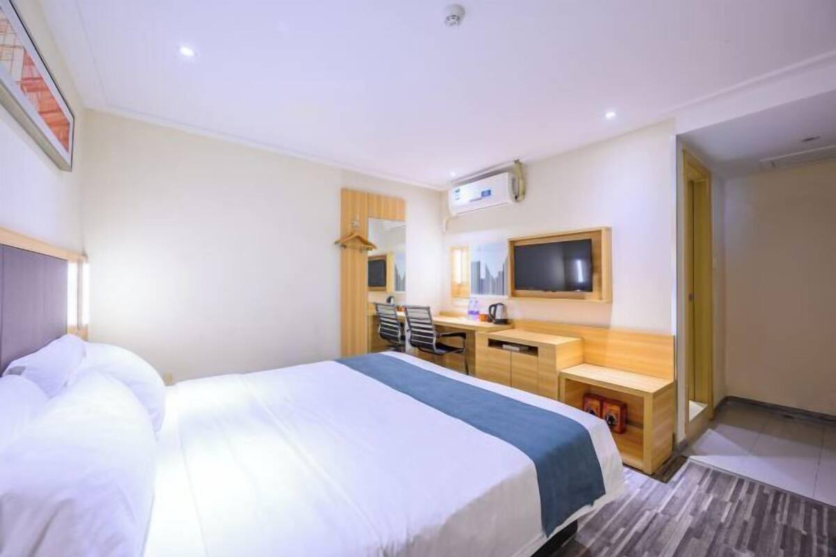 A hotel room with a large bed, a desk, a chair, a TV, and a mirror.