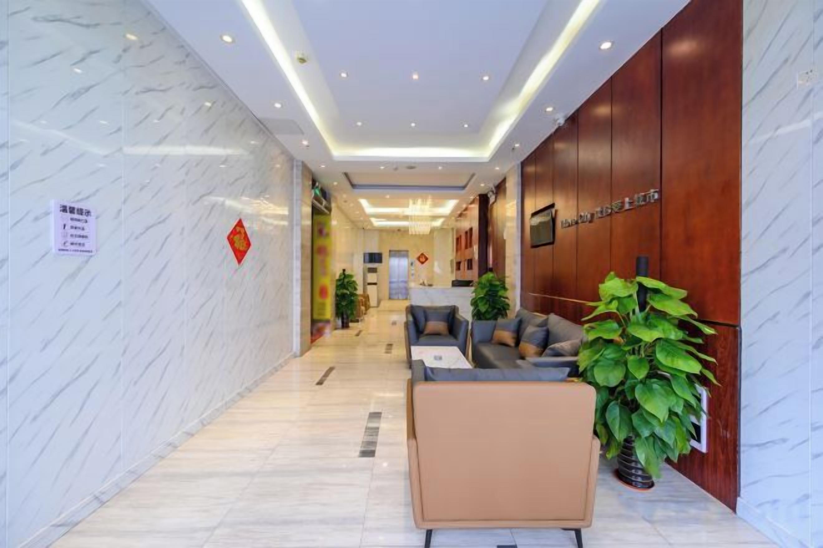 A hotel lobby with marble walls, a reception desk, seating area, and potted plants.