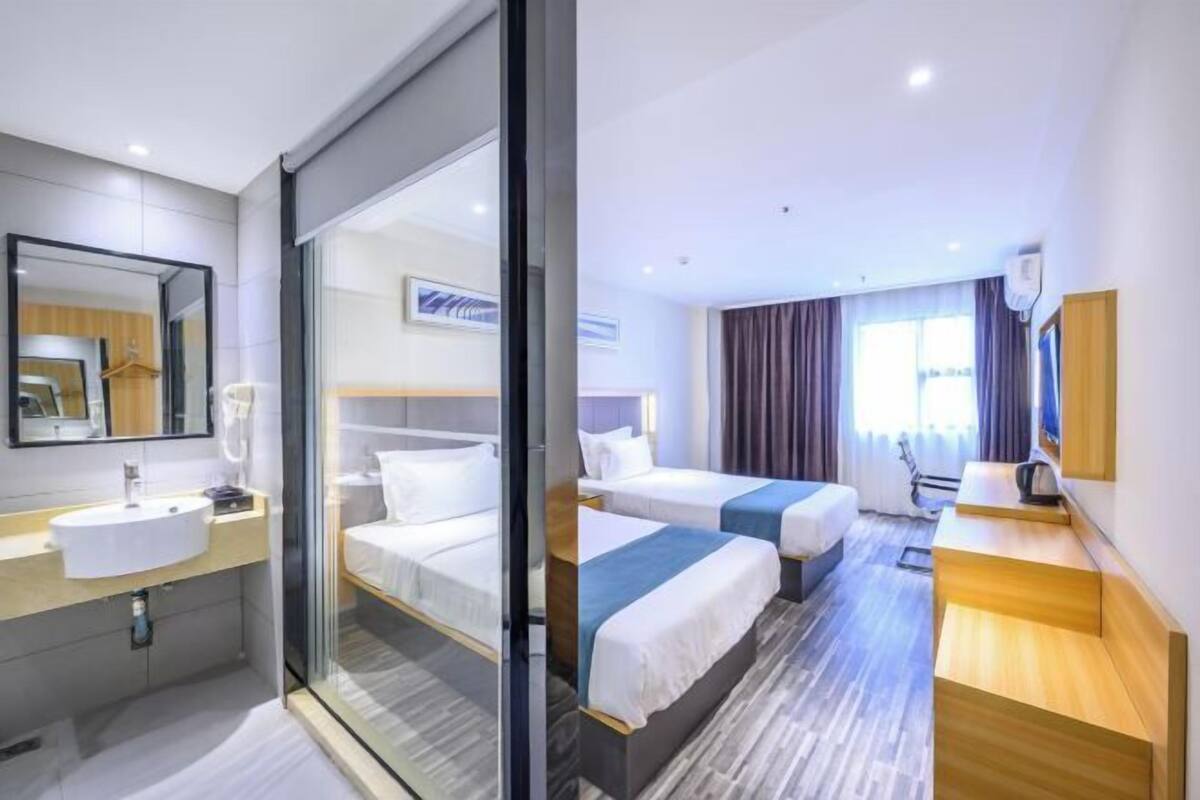 A hotel room with a glass partition, a bed, a bedside table, a desk, and a window with curtains.