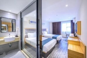 Ein Hotelzimmer mit Glastrennwand, einem Bett, einem Nachttisch, einem Schreibtisch und einem mit Vorhängen versehenen Fenster.