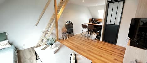 A loft-style room with a wooden floor, a dining area with a table and chairs, a staircase, and a sliding door.