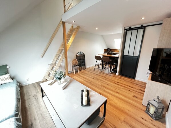 Un espacio tipo loft con piso de madera, una zona de comedor con mesa y sillas, una escalera y una puerta corredera.
