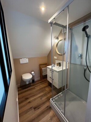 Un baño moderno con cabina de ducha de vidrio, inodoro y tocador con espejo.
