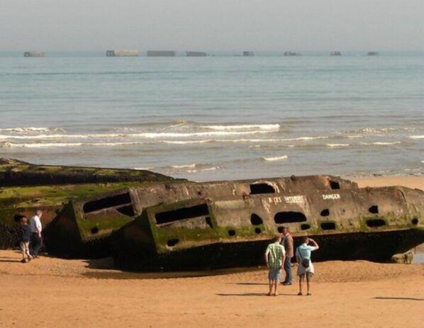 Un gran naufragio oxidado sobre una playa arenosa, con el océano al fondo.