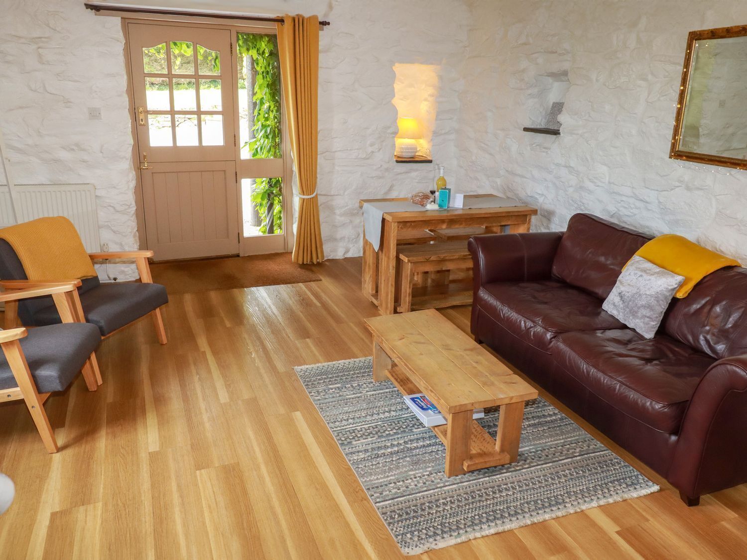 A cozy living room with a brown leather sofa, wooden chairs, a wooden coffee table, and a small wooden desk.