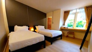 Quarto de hotel com duas camas, uma escrivaninha, uma janela com cortinas e um banquinho pequeno.