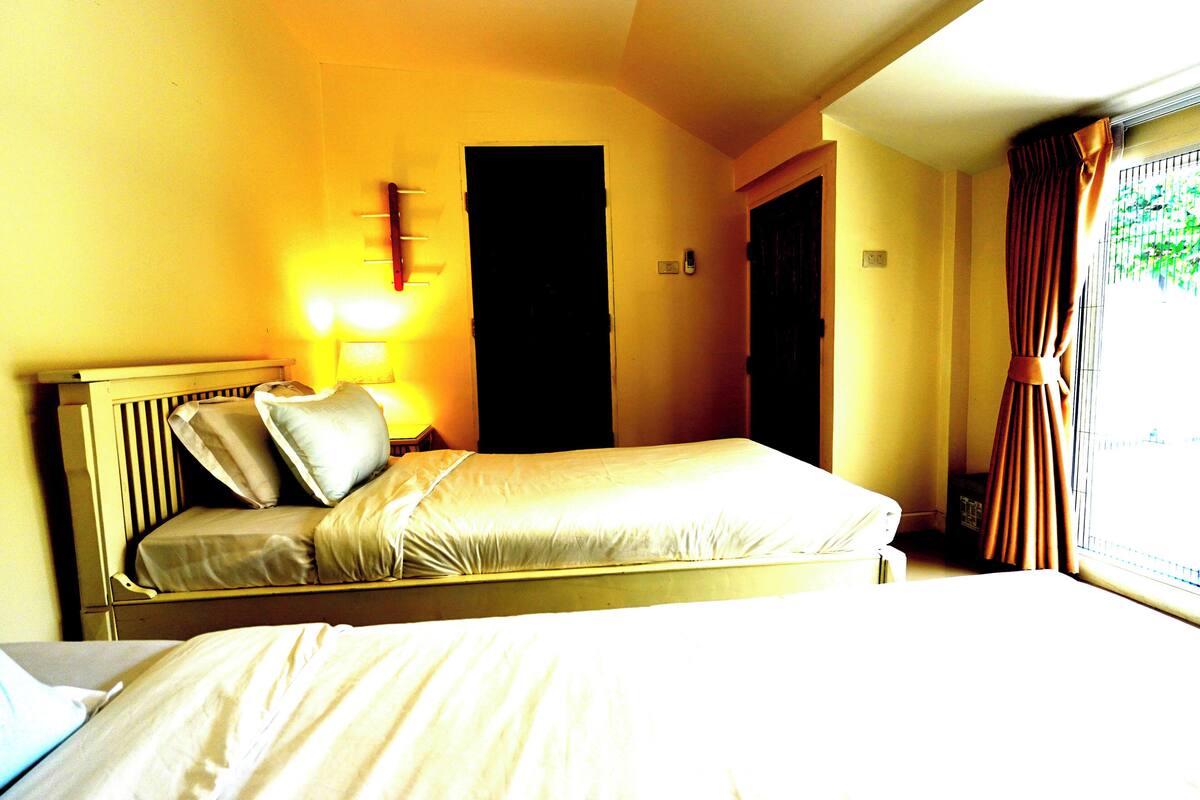 A single bed with a headboard, a bedside table with a lamp, and a window with curtains.