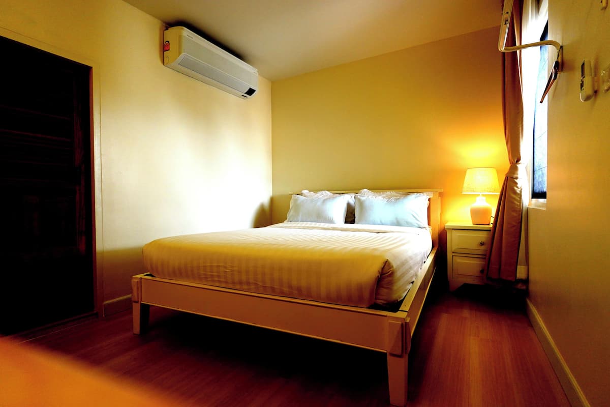A hotel room with a bed, bedside table, lamp, and an air conditioning unit.