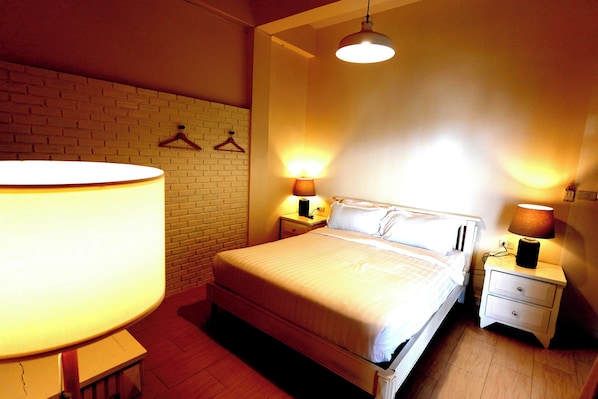 A neatly made bed with a white comforter and pillows, a bedside table with a lamp, and a hanging light fixture above the bed. - To The Moon Guesthouse (Chiang Mai)