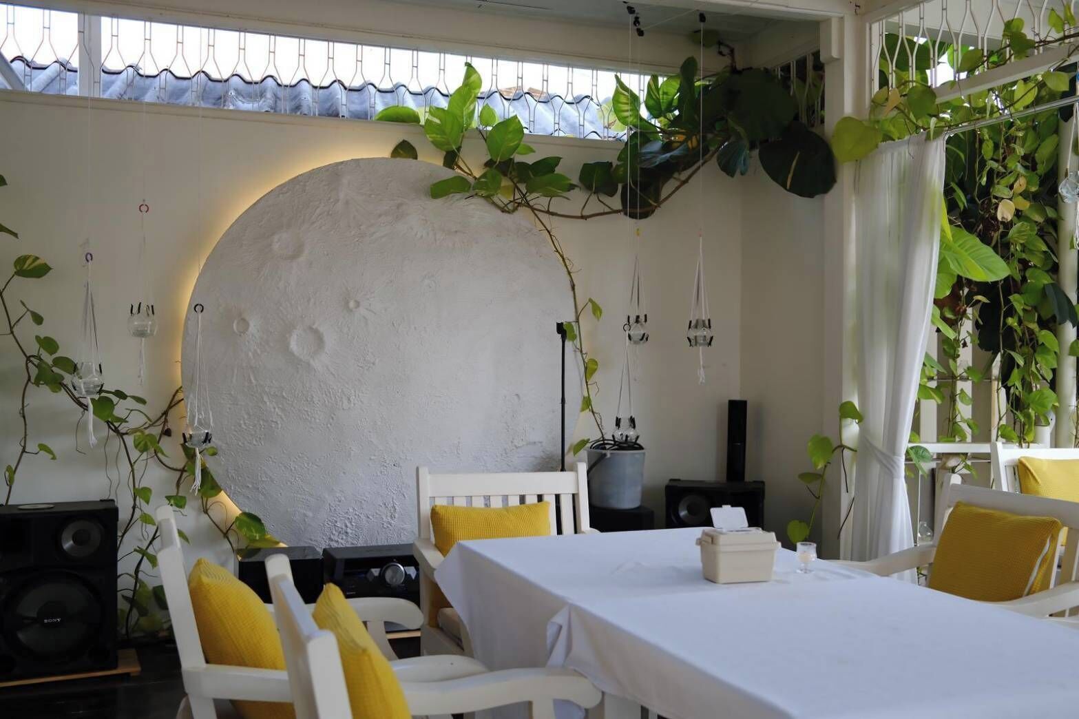 A dining area with a round white wall, white chairs with yellow cushions, and a table set for two.