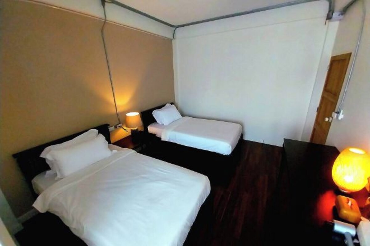 A hotel room with two beds, a nightstand with a lamp, and a wooden floor.