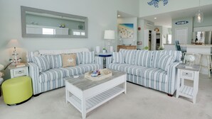 A living room with striped sofas, a coffee table, and a bright green ottoman.