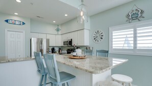 A kitchen with white cabinets, a central island with stools, a clock, and a sign that says "NO CRABBY BEACH".