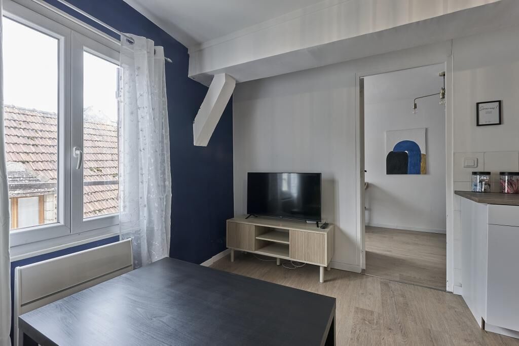 Un appartement moderne doté d’un téléviseur posé sur un meuble en bois, d’une table à manger et d’un coin cuisine.