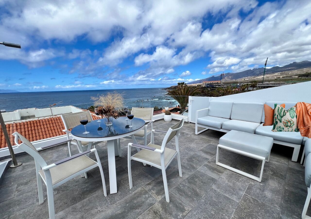 Eine Terrasse mit Tisch, Stühlen und einer Sitzecke, mit Blick aufs Meer.
