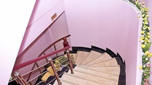 Una scala a chiocciola con una parete rosa e una composizione floreale decorativa sulla destra.