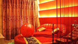 Una stanza con un letto rosso, un grande palloncino rosso e una tenda con motivo floreale.