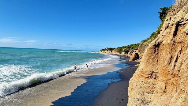 Una playa con aguas azules cristalinas, una orilla de arena y un acantilado rocoso.