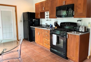 Una cocina con armarios de madera, un refrigerador negro, un microondas, una estufa y un tostador.