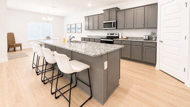 A modern kitchen with a central island, bar stools, grey cabinets, and a microwave. - 4 BR/3BA (2K, Q, 2T) New Construction.  Pet friendly (Foley)