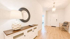 A hallway with a wooden console table, a lamp, a mirror, and a chair. - 4 BR/3BA (2K, Q, 2T) New Construction.  Pet friendly (Foley)
