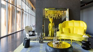 A modern interior with a bright yellow sofa, a large chandelier, and a reflective sculpture.
