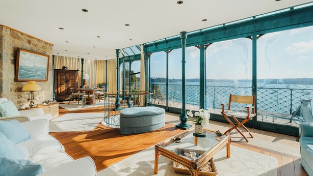 Un balcón amplio con vistas al mar, amueblado con un sofá, reposapiés y sillas, y un comedor con mesa y sillas.