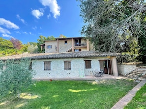 Un edificio in pietra con tetto in tegole, un piccolo patio con tavolo e sedie, e un prato.