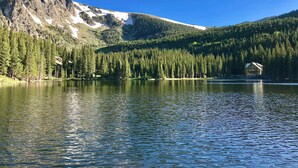 Una cabaña junto a un lago con montañas al fondo.