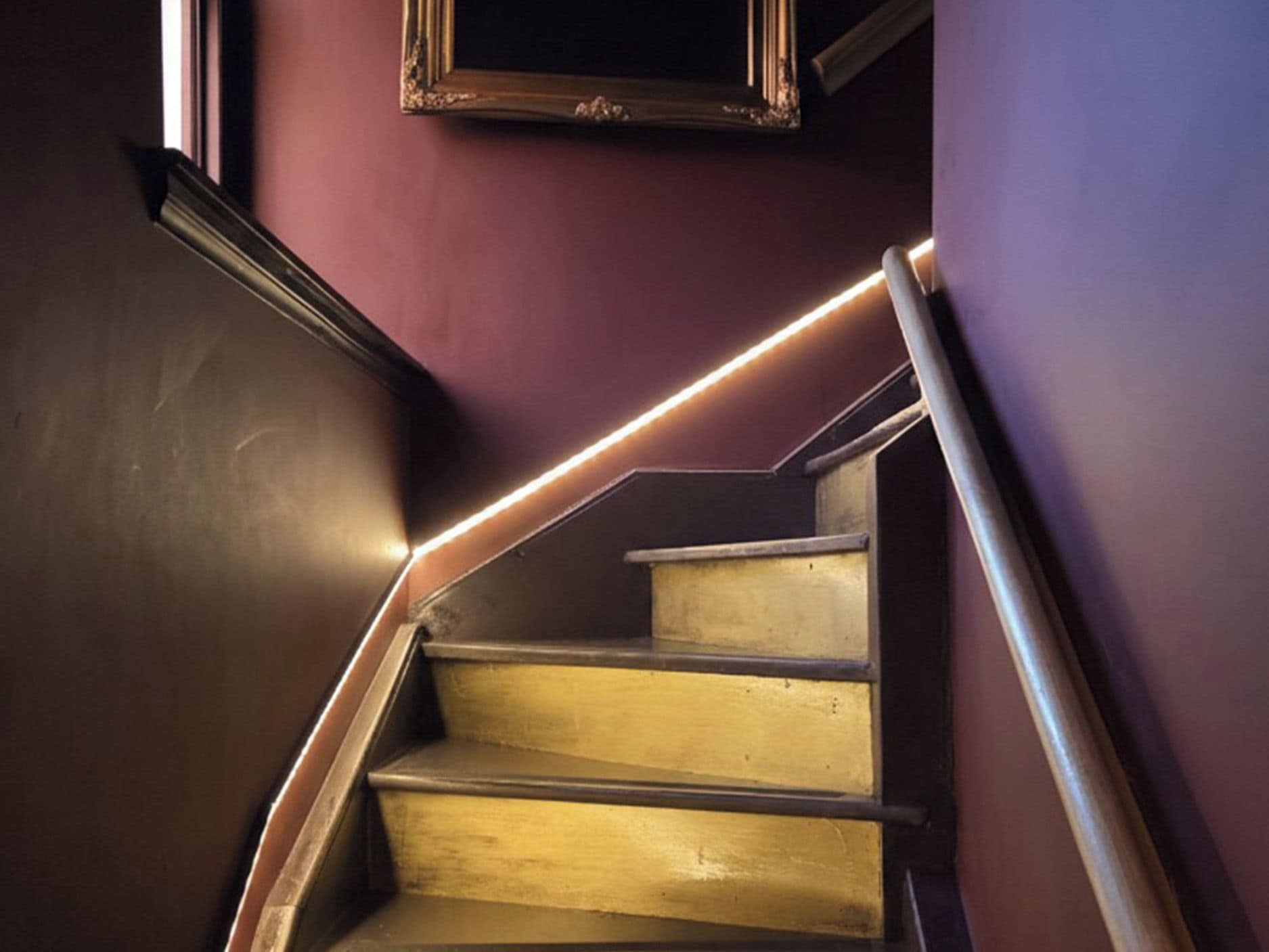 Eine Treppe mit Holzboden und Metallgeländer, die zu einer dunklen Wand mit einem gerahmten Bild führt.