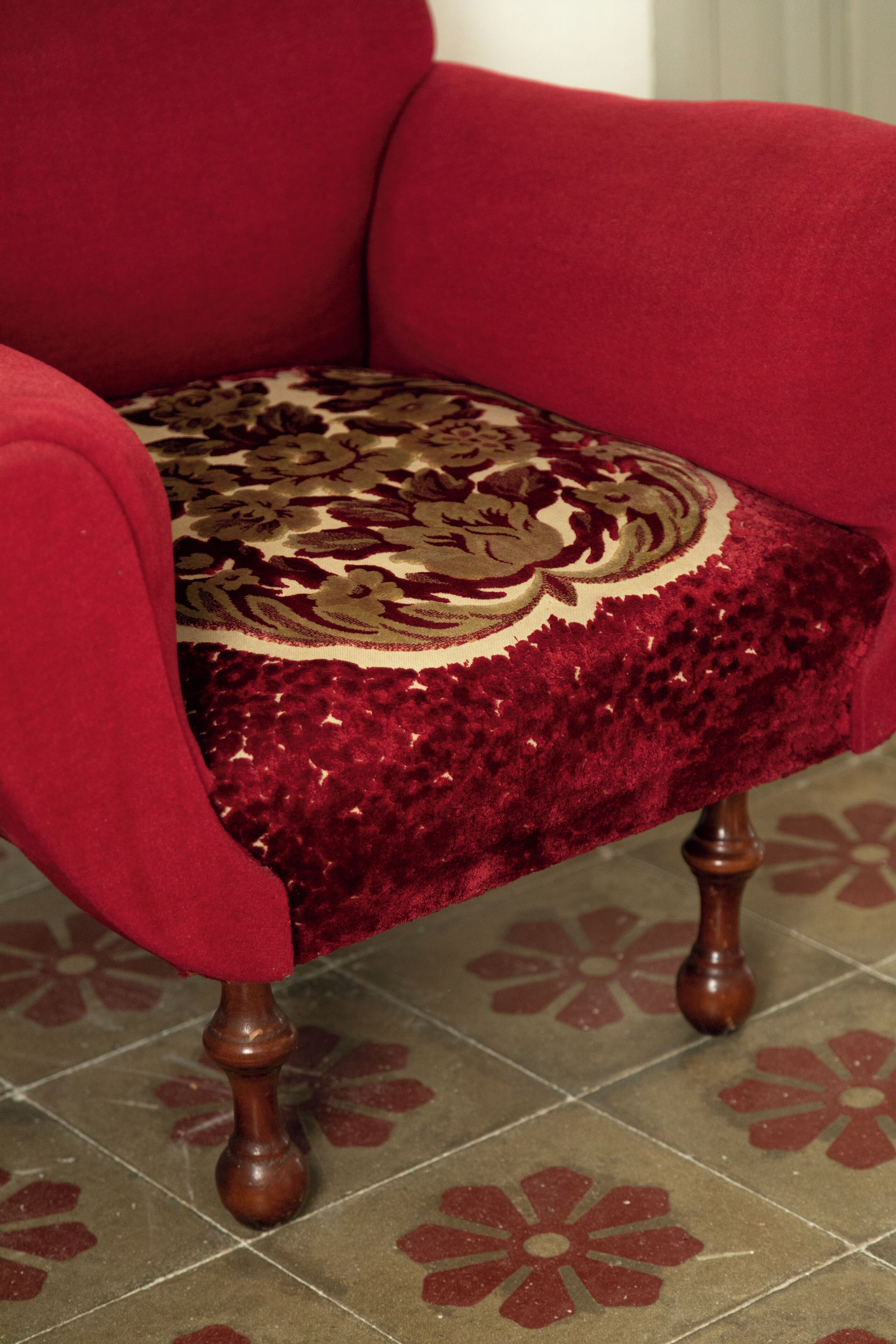 A red armchair with a patterned cushion and wooden legs.