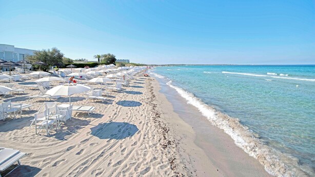 Una platja amb gandules i ombrel·les, un cel blau clar i una mar tranquil·la.