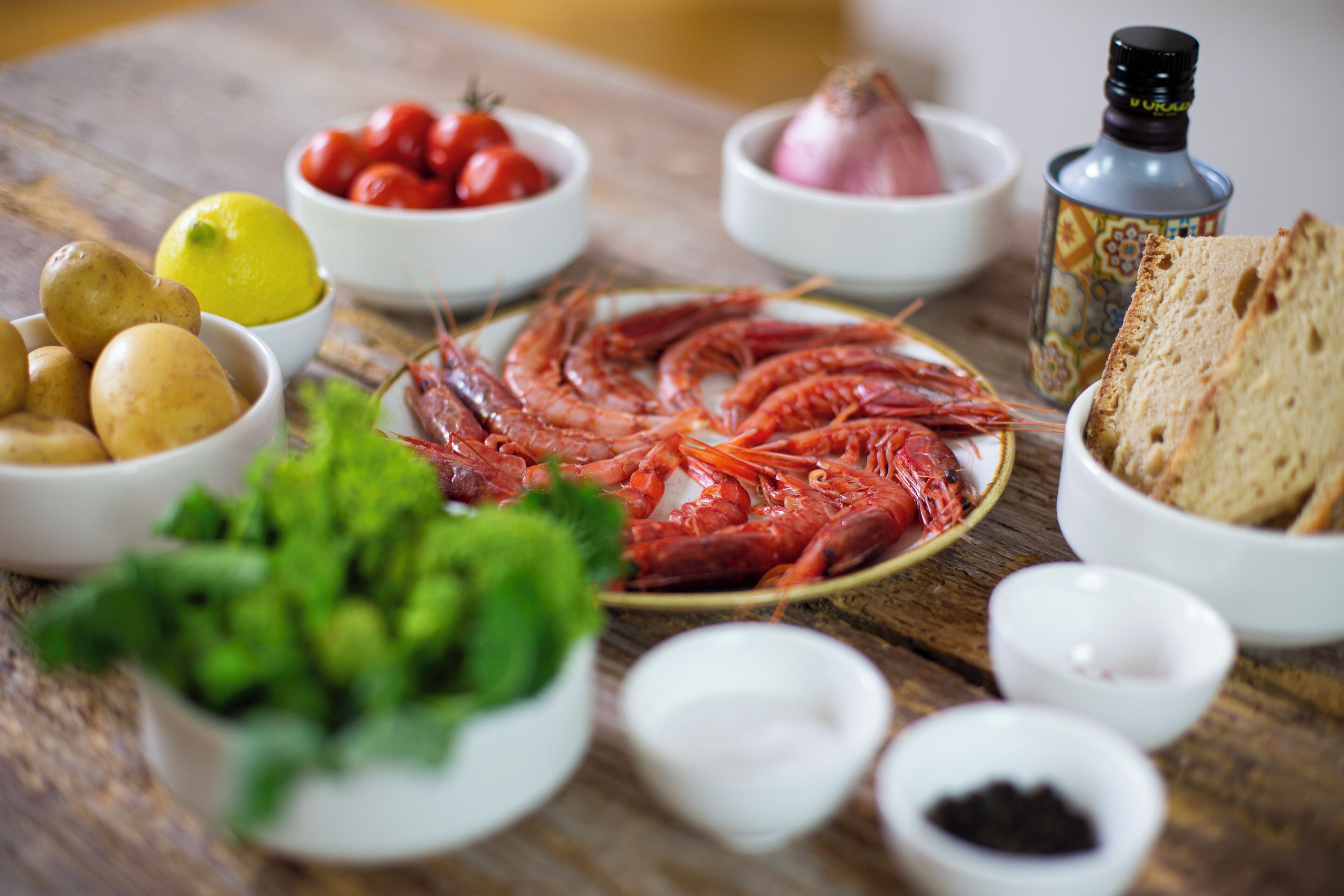 A wooden table with various food items including shrimp, potatoes, tomatoes, lemon, and bread.