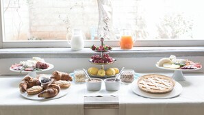Buffet de l'esmorzar amb diversos pastissos, fruites i begudes sobre una taula al costat d'una finestra.