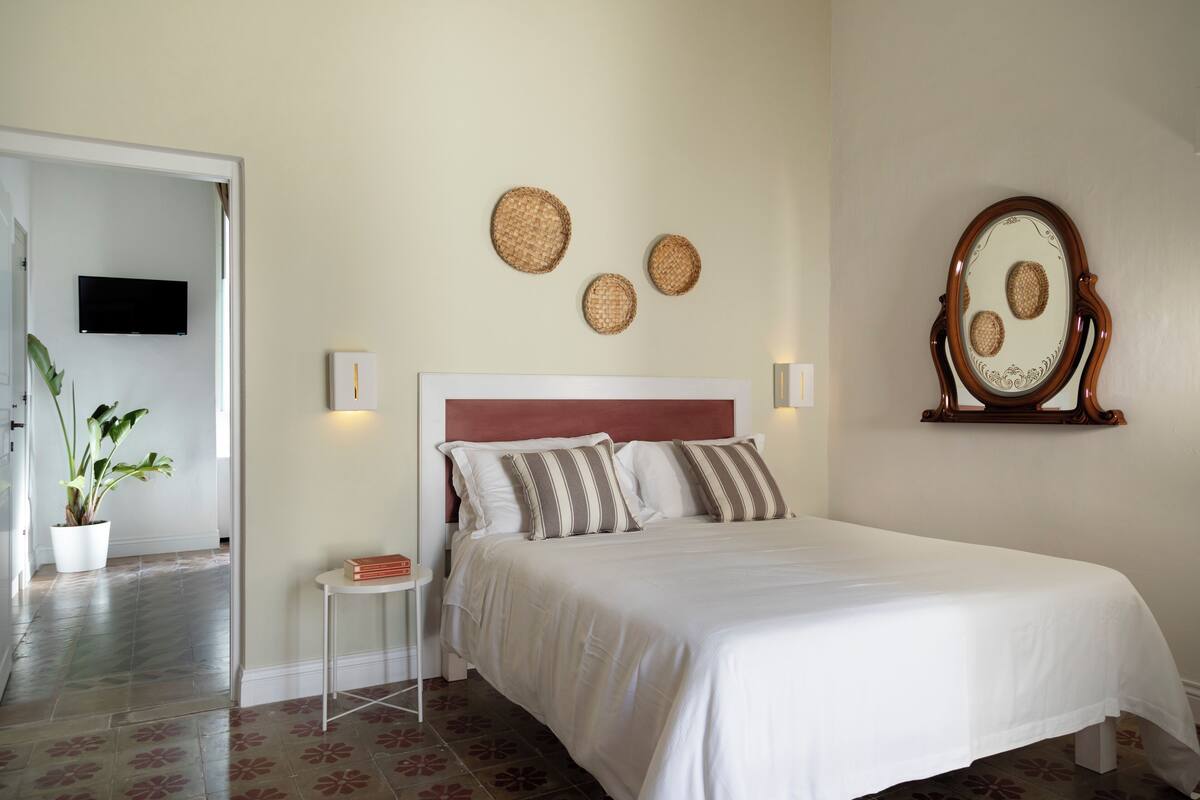 Un dormitorio con una cama, una mesita de noche, una planta en maceta, un televisor montado en la pared y decoración mural.