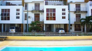 Un edificio moderno de varios pisos con balcones, piscina y automóviles estacionados.