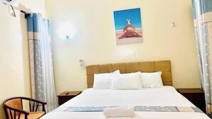 Una habitación de hotel con cama, una silla, mesita de noche y aire acondicionado de pared.