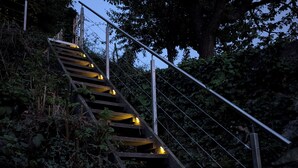 Un escalier en bois avec des rampes en métal, entouré de verdure et d’arbres, qui monte une colline.