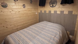 A bedroom with a bed, wooden walls, a ceiling light, a window with curtains, and wall decorations.