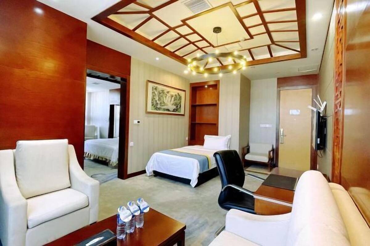 A hotel room with a bed, two chairs, a small table, and a ceiling light fixture.
