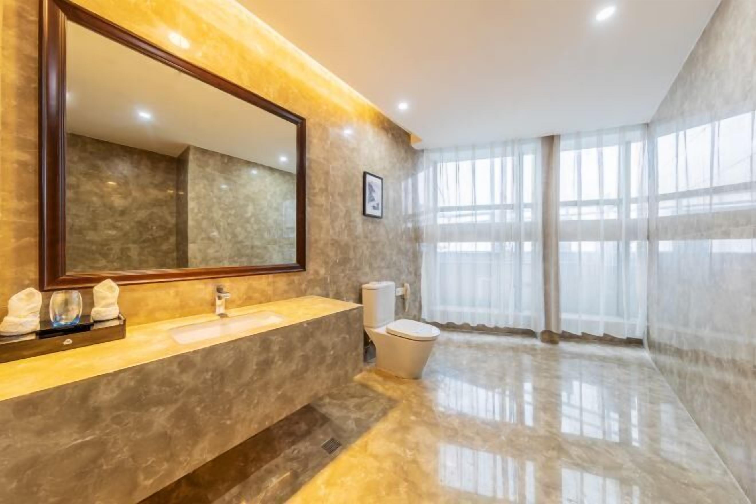 A modern bathroom with a large mirror, a marble sink, and a toilet.